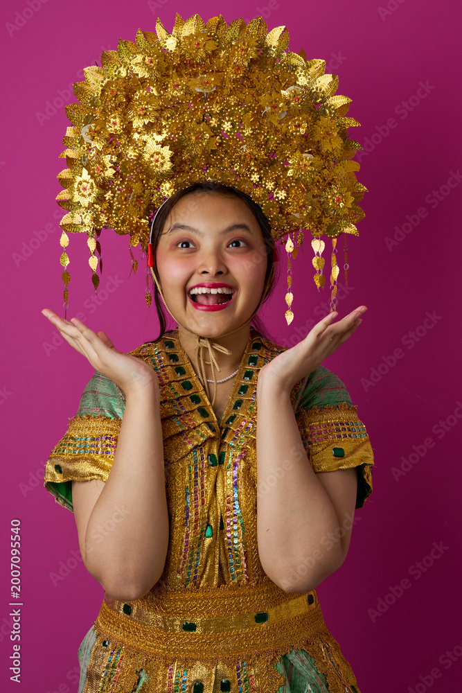Fototapeta premium Joyful Young Indonesian Asian Girl Wearing Ornate Gold Headdress and Traditional Costume for Cultural Celebration