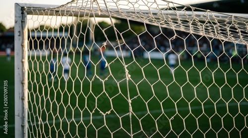 Close-up of a soccer goal net with blurred players in the background.