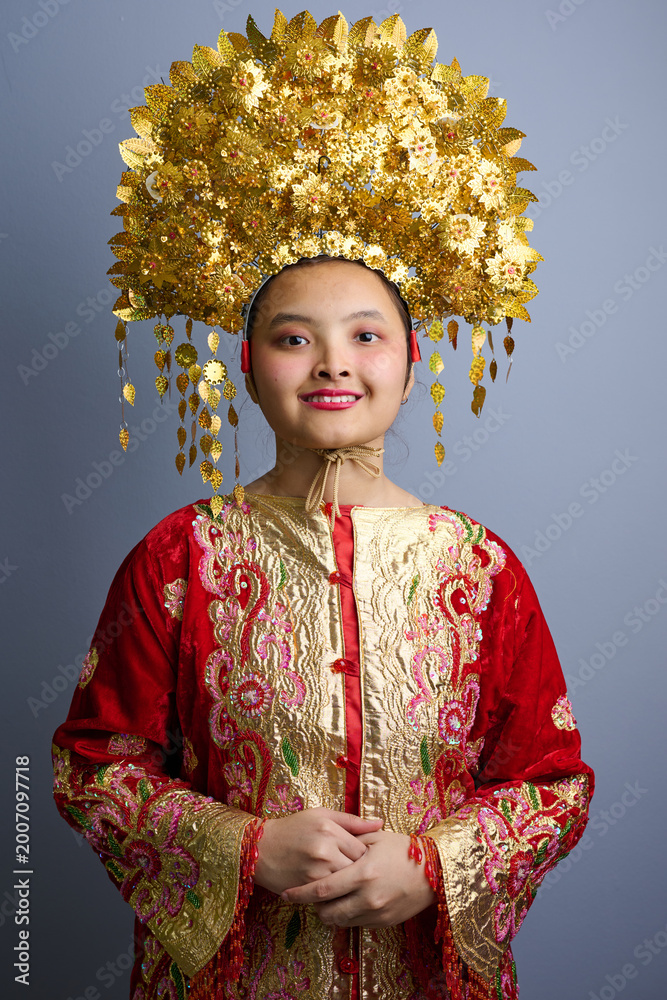 Fototapeta premium Young Indonesian Asian Woman Wearing Traditional Gold Headdress and Embroidered Red Costume Smiling