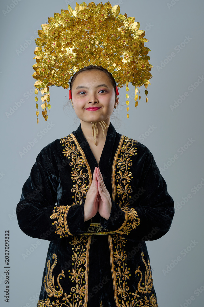 Fototapeta premium Portrait Of A Young Indonesian Asian Woman Wearing A Gold Traditional Headdress And Embroidered Black Costume