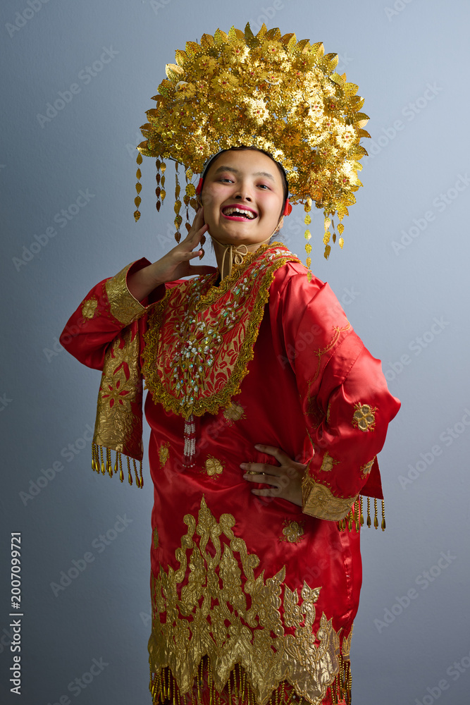 Fototapeta premium Young Indonesian Asian Woman in Red and Gold Traditional Costume With Ornate Gold Headdress Portrait