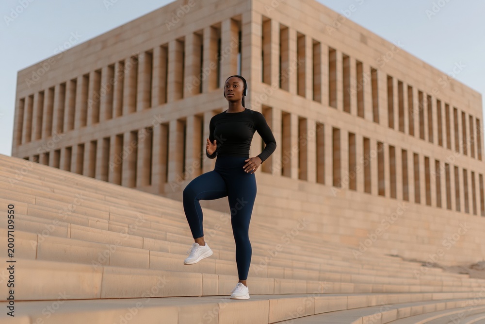 Fototapeta premium Black woman training on modern urban stairs, focused on fitness and running drills, strong, determined and energetic city workout session