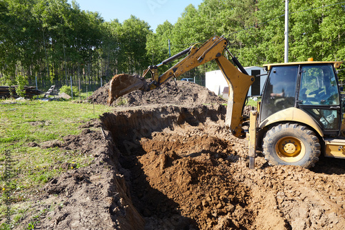 Tableau sur toile Backhoe excavator digging a deep trench at a construction site, moving soil to p
