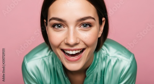 Portrait of a happy young woman with a wide smile, looking directly at the camera with bright eyes, her face framed by her hair and shoulders, close-up shot against a pastel pink background