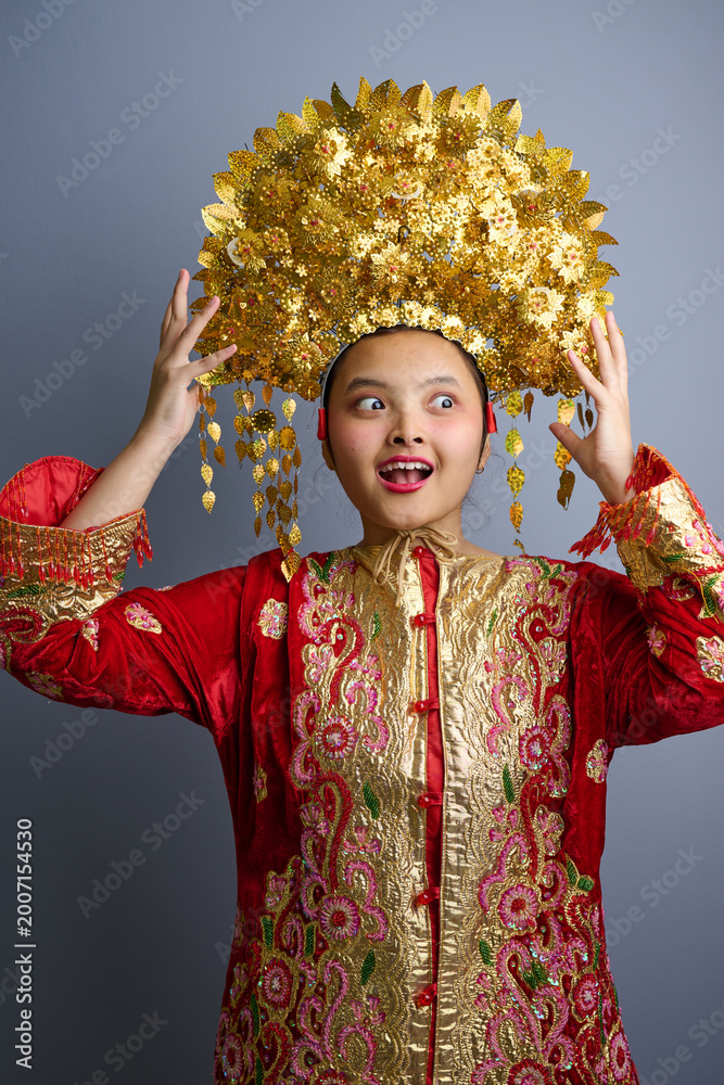Fototapeta premium Young Indonesian Asian Woman Wearing Traditional Gold Headdress and Red Embroidered Costume for Cultural Celebration