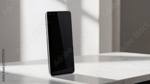 Smartphone stands angled on marble surface.
​Glossy black screen reflects bright light.
​Modern device featuring dual front cameras.
​Sleek metallic frame with minimalist design.
​Natural sunlight
