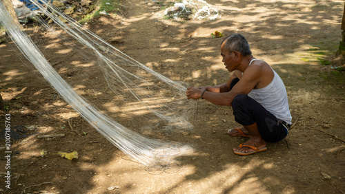Obraz na plátně Traditional Indonesian fisherman mending and repairing fishing net in Malang, East Java