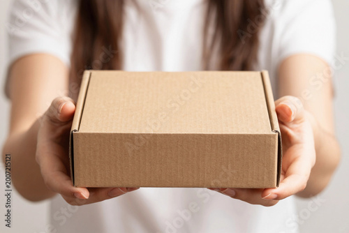 Person holds cardboard box gently, offering it forward.