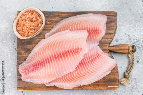Fotografija Raw tilapia fillets on wooden cutting board with sea salt, fresh freshwater fish from aquaculture on light background