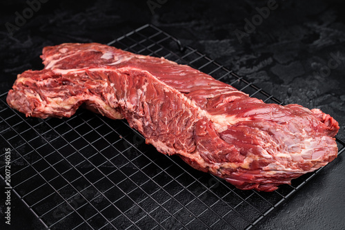 Closeup raw onglet hanger steak on metal grate over black textured surface, rich red meat with visible fibers and fat, ideal for barbecue and cooking