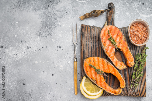 Fotografie Grilled sockeye salmon steaks  on wooden board with thyme lemon and salt, light