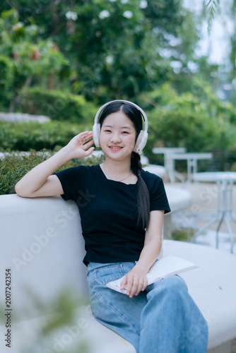 Tableau sur toile Smiling Young Woman Wearing Headphones Using Smartphone in Park