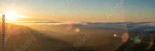 Sunrise over mountains with clouds and sun rays shining brightly in the sky at dawn or dusk