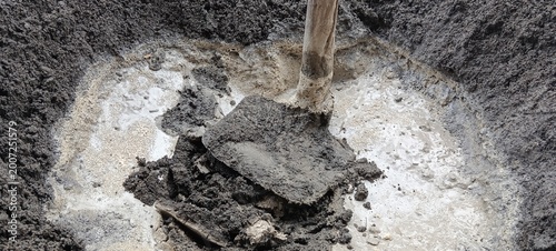 Foto shovel mixing wet cement mortar with sand and water in a pit, showing muddy texture and manual construction process