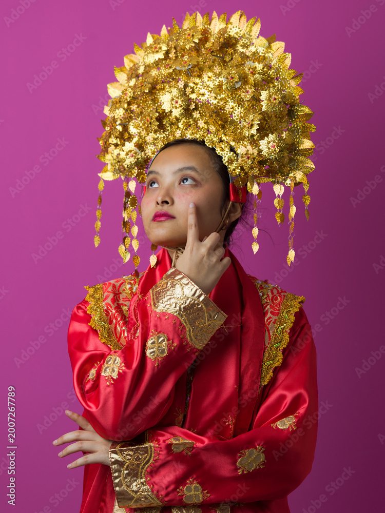 Fototapeta premium Young Indonesian Asian Woman Wearing Traditional Gold Headdress And Red Embroidered Costume Portrait For Celebration