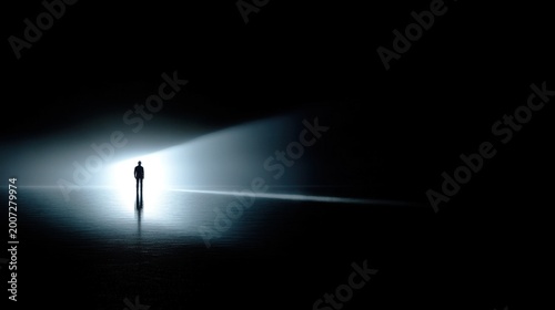 A lone silhouette stands in a vast dark expanse, illuminated by a narrow beam of cool light, reflecting on a smooth surf