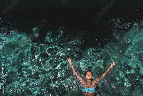 Woman with arms outstretched floating in villa pool, Uluwatu, Bali