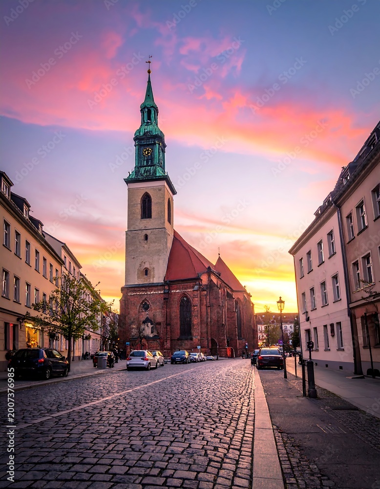 Fototapeta premium Historic cobblestone street leads to a church steeple at sunset