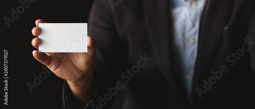 Businessman holding blank white business card with copy space on dark background, ideal for branding, corporate identity, marketing, and presentation design