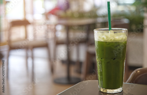 Iced matcha green tea latte in a glass with straw on table in cafe, soft light and blurred background with copy space