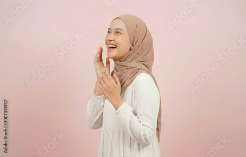 Happy Muslim woman looking sideways and shouting with hands near mouth against pink background