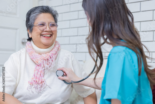 Senior woman smiles during health checkup while nurse uses stethoscope