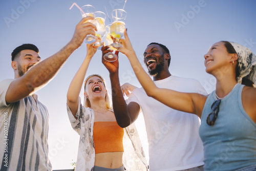 Diverse friends cheering with cocktails having fun outdoors