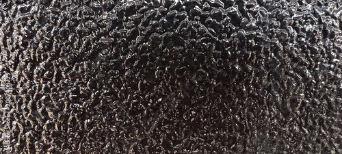 Slika na platnu Close-up of a dark glossy surface with irregular bumps and ridges, creating a shimmering effect under reflected light
