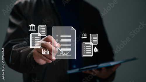 Professional man wearing dark jacket signs digital document holding pen manages financial icons bank graph percentage money bag indoors against dim background throughout corporate business legal.