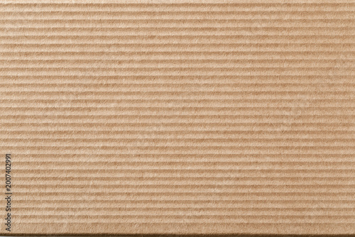 Detailed close-up texture of recycled brown corrugated cardboard packaging material featuring horizontal ridges and a natural organic fibrous surface for background and design.
