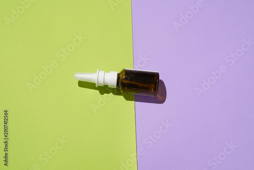 Amber glass nasal spray bottle on a diagonal green and purple background with sharp shadow