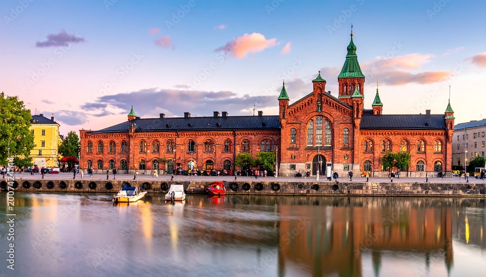 Fototapeta premium Ornate brick building on waterfront at sunset with boats and reflections