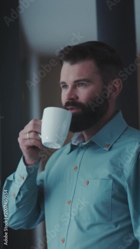 Person with beard drinking coffee indoors, Relaxed male with beard enjoying cup of coffee by softly lit window