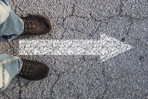 Feet standing on asphalt with white direction arrow forward road marking decision concept top view