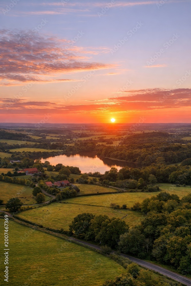 Naklejka premium Stunning sunset over serene lake. Vibrant colors fill sky and reflect on water. Peaceful landscape inspires relaxation and tranquility. Ideal image for nature lovers and travel enthusiasts.