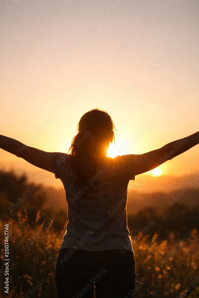 Fototapeta premium Silhouette of woman enjoying sunset in nature. Peaceful atmosphere creates sense of freedom and tranquility. Vertical image captures beauty and joy of outdoor lifestyle.