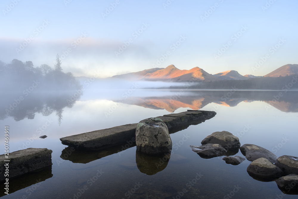 Obraz premium Calm reflections of mountains in lake on misty morning: Catbells and Derwentwater, Lake District, UK.