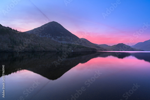 Pink sunrise reflections of Grasmoor at Crummock Water in The Lake District, UK.