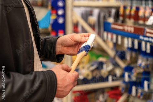 Caucasian professional painter prepares brush for job, hands loading bristles with paint, readying tool for application on renovation site, focused practical moment in store aisle