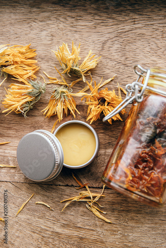 Making homemade Calendula officinalis common marigold cold infusion oil in glass jar and handmade medicinal salve in metal jar. Above view.