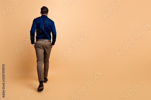 Obraz na płótnie Business casual man walking away in studio on beige background, rear view of a c