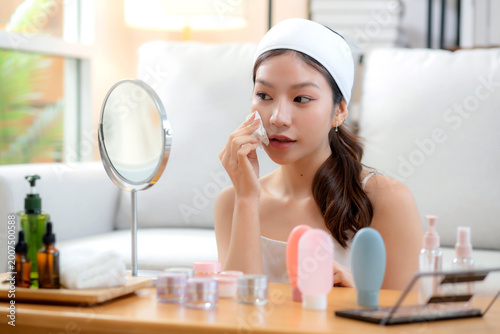 Beautiful young asian woman smile with skin care use oil blotting paper on face looking mirror in the room, beauty woman happy and clean makeup and cosmetic with tissue, skincare and health