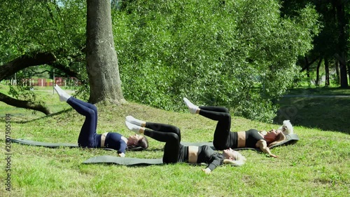 Friends enjoying quality time on exercise mats surrounded by nature. Young women training in park. Fitness concept. 4K, UHD