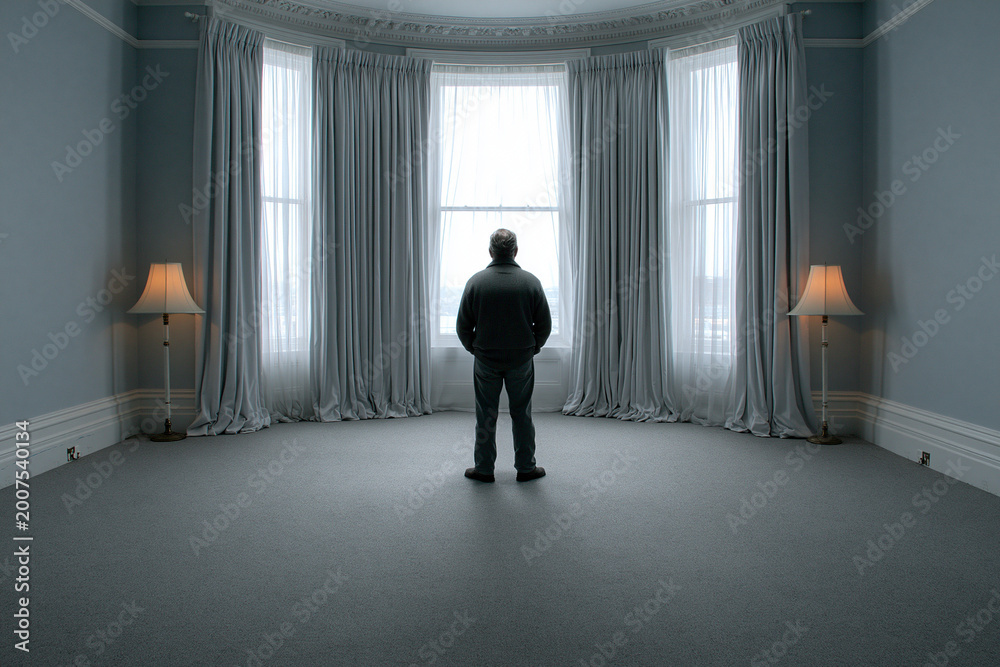 Fototapeta premium Man standing alone in empty room looking through large window