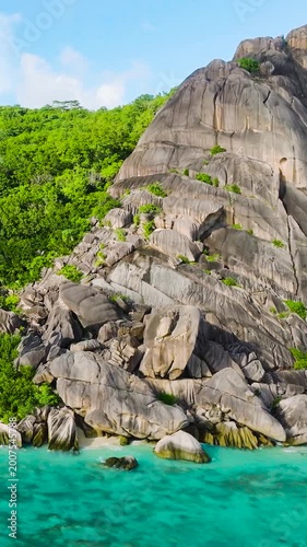 Granite rock formations with dense greenery along the beach and clear waters. La Digue, Seychelles.