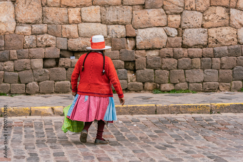 An indigenous peruvian woman walking across a cobblestone street in Cusco, Peru
