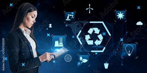 Businesswoman using digital tablet with futuristic eco energy icons and recyc...