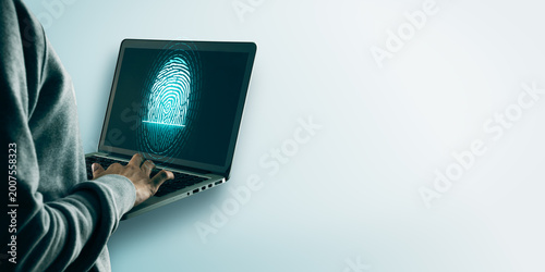 Person using laptop with glowing fingerprint login on screen against soft lig...