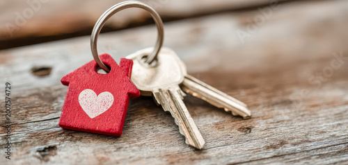 Keys with a red house charm on a wooden surface for new home ownership and personal beginnings in life journey