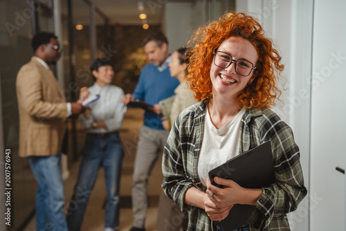 Happy red-haired woman smiling at diverse office team